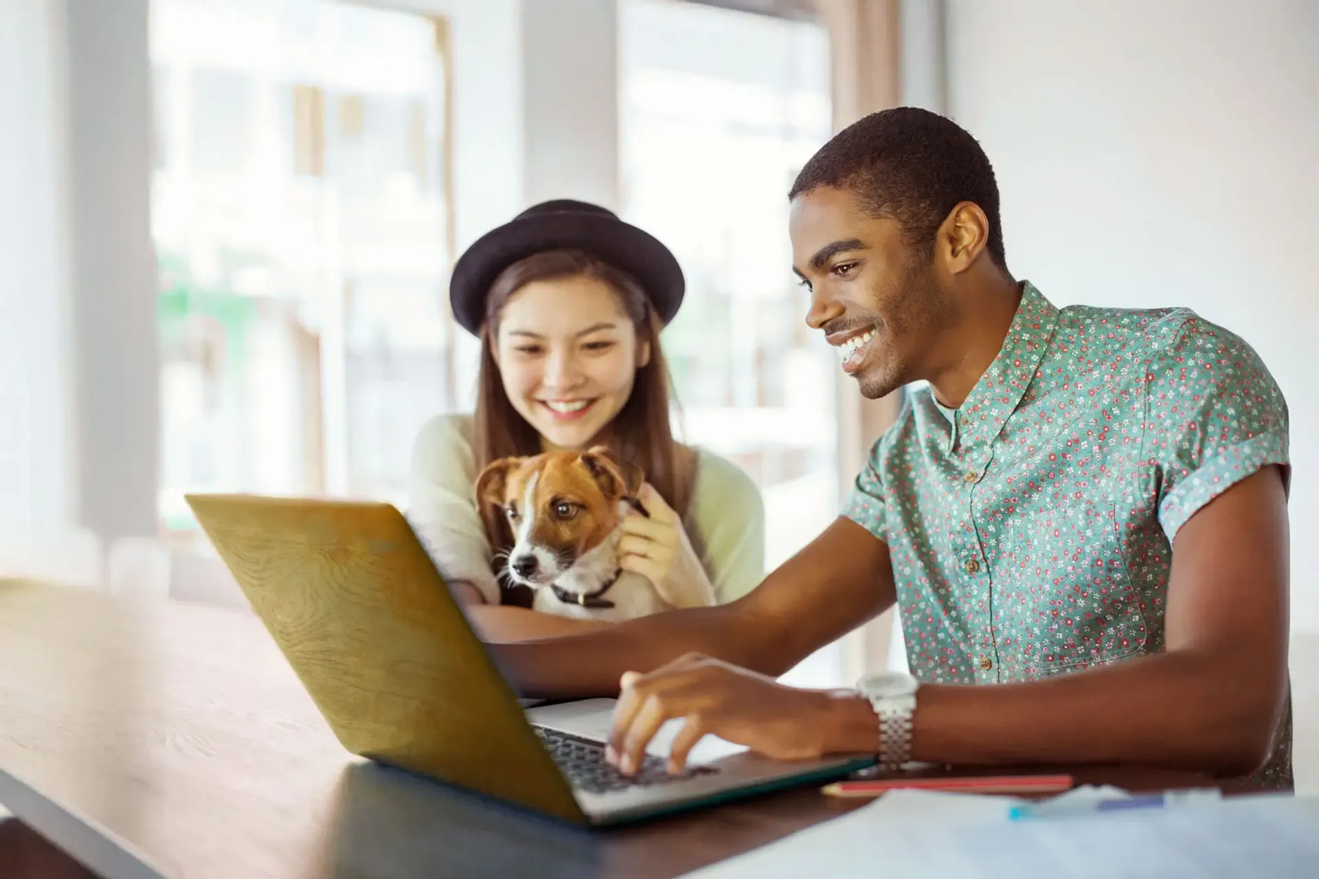 A smiling woman and man enjoy their work. The woman cuddles with a small, cute dog.
